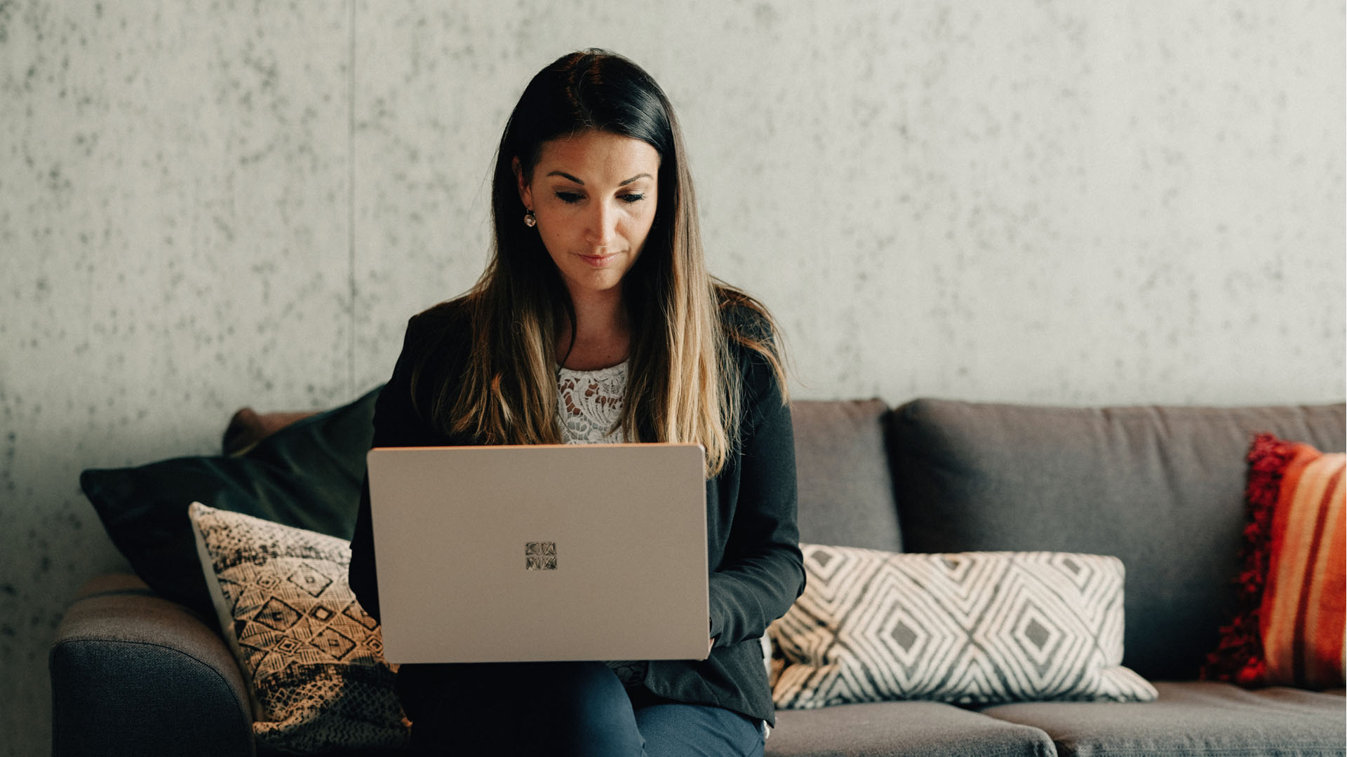 Eine Frau sitzt auf dem Sofa und arbeitet mit dem Modern Workplace Laptop